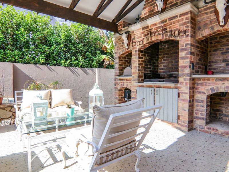 Covered outdoor patio featuring a substantial built-in brick braai, exposed timber rafters, and durable terrazzo flooring, ideal for alfresco dining and entertaining.