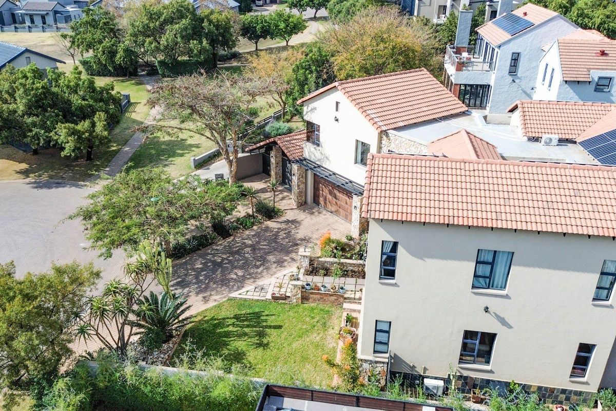 An aerial view of a multi-story residential property featuring terracotta roof tiles, solar panels, a paved driveway, and established garden landscaping.