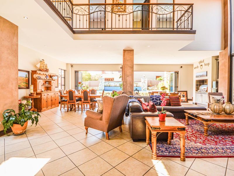 Spacious open-plan living and dining area featuring a mezzanine level with wrought iron balustrade, tiled flooring, and large bi-fold doors opening to the outdoors.