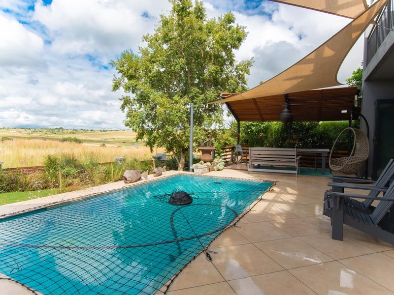 Outdoor pool area featuring a tiled patio, timber pergola with shade sail, and a swimming pool with a safety net, overlooking open fields.