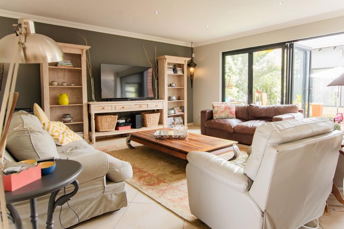 A well-lit living room featuring tiled flooring, crown molding, and bi-fold doors that provide seamless access to the outdoor area.