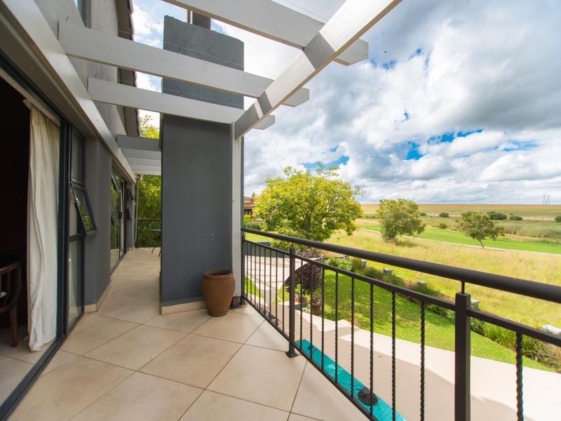 A spacious covered balcony featuring tiled flooring, a metal balustrade, and a timber pergola, offering scenic views of the surrounding landscape.