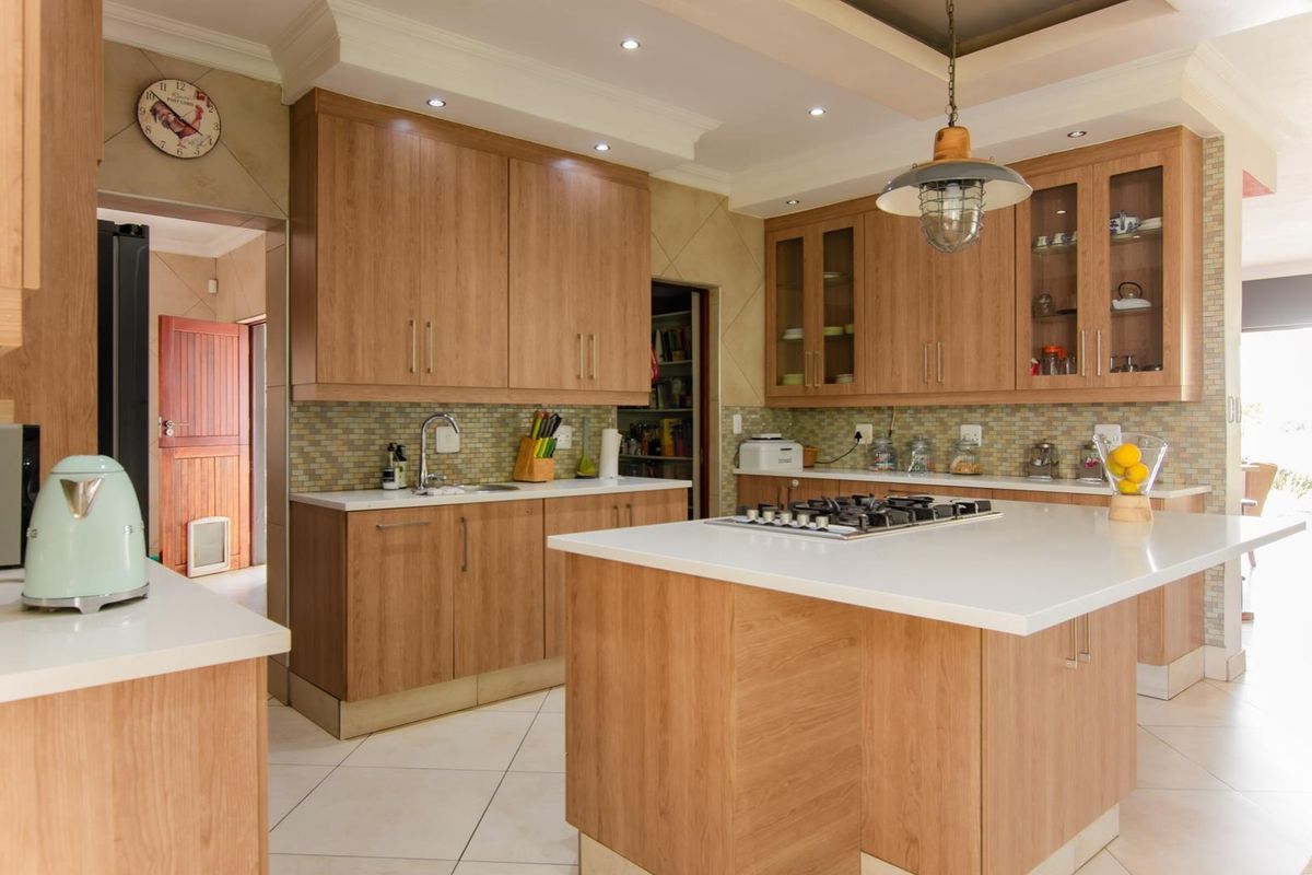 Spacious kitchen featuring wood-finish cabinetry, a central island with a gas cooktop, stone countertops, and a mosaic tile backsplash with an adjoining pantry.