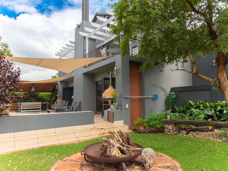 Rear exterior view featuring a landscaped garden, a tiled patio area with a built-in pizza oven, and an upper-level balcony with a pergola.