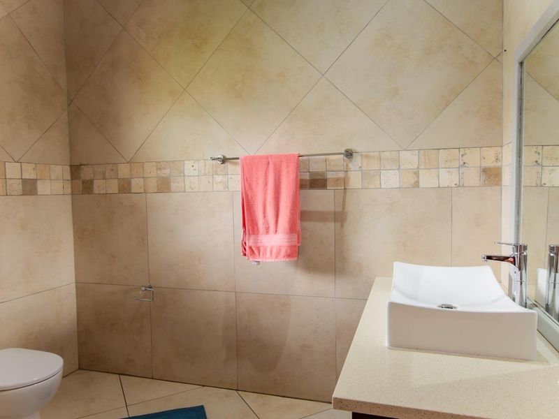 A well-maintained bathroom featuring neutral ceramic wall and floor tiles, a modern vessel sink on a stone vanity, and a wall-mounted mirror.