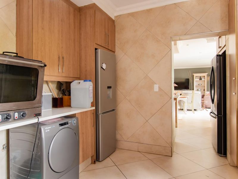A functional scullery area featuring built-in wooden cabinetry, tiled flooring, and wall tiling, providing additional storage and utility space adjacent to the main living area.