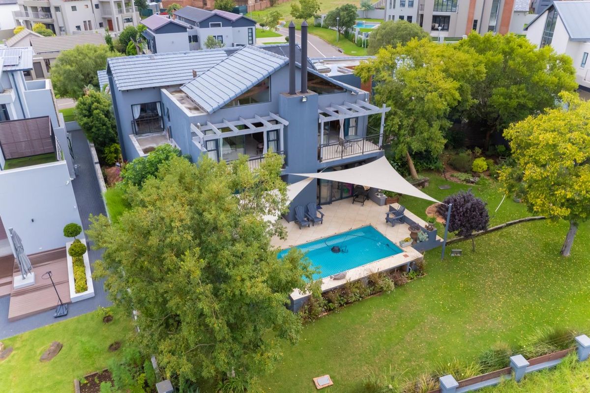 Aerial view of a modern residential property featuring a tiled roof, swimming pool, patio with pergola, and a spacious landscaped garden.