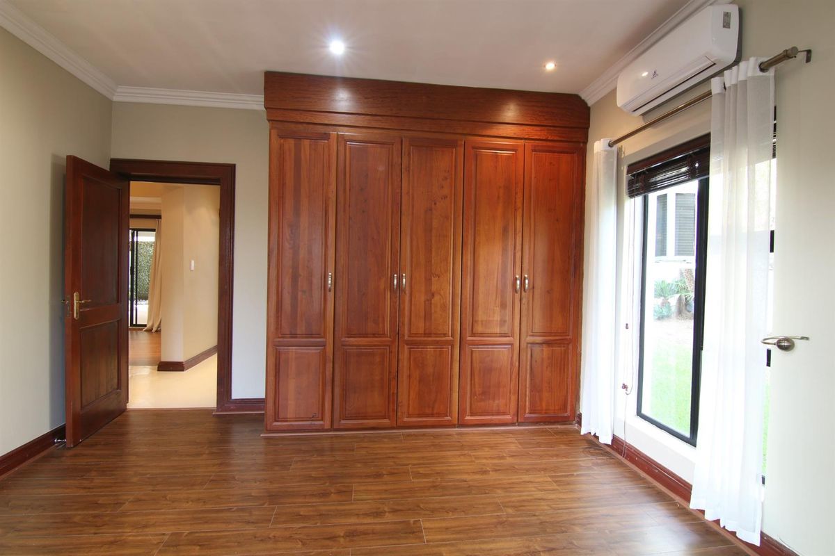 Spacious bedroom featuring warm-toned laminate flooring, extensive built-in wooden cabinetry, and a wall-mounted air conditioning unit.