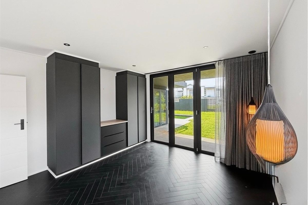 Modern bedroom featuring dark herringbone flooring, built-in matte cabinetry, and large glass sliding doors providing direct access to the rear garden.