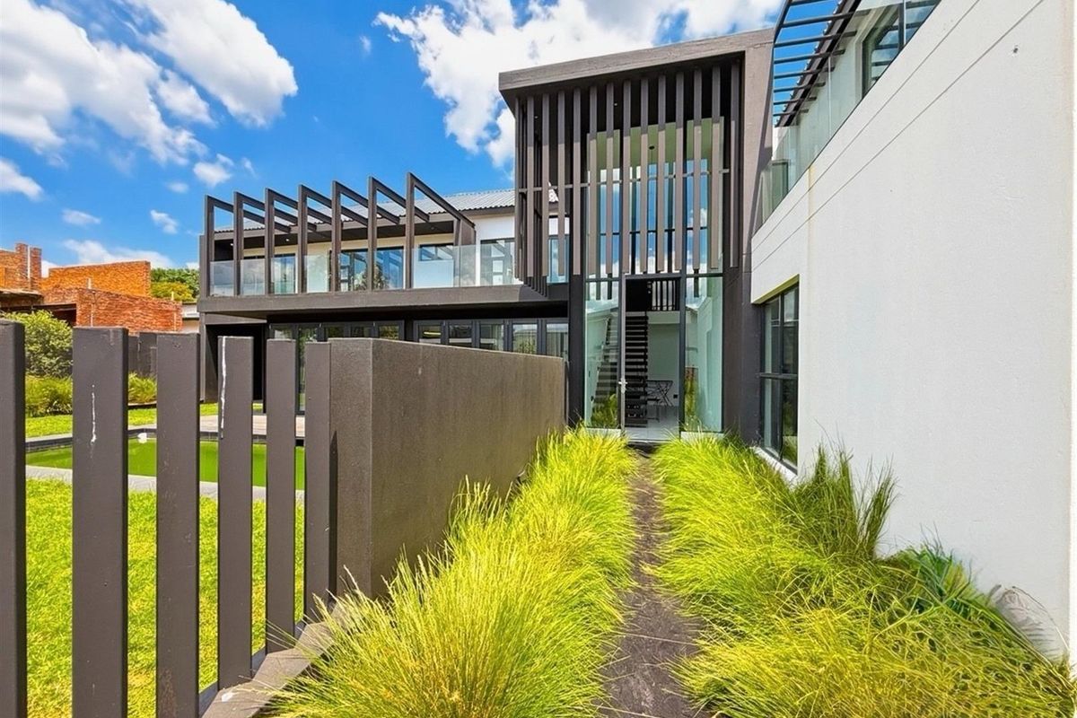 Modern architectural rear facade featuring clean lines, glass balustrades, vertical timber screening, and a landscaped garden pathway.