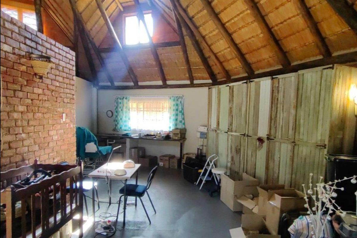 A rustic bedroom or multi-purpose space featuring a high exposed thatch roof, brick feature wall, and built-in timber cabinetry.