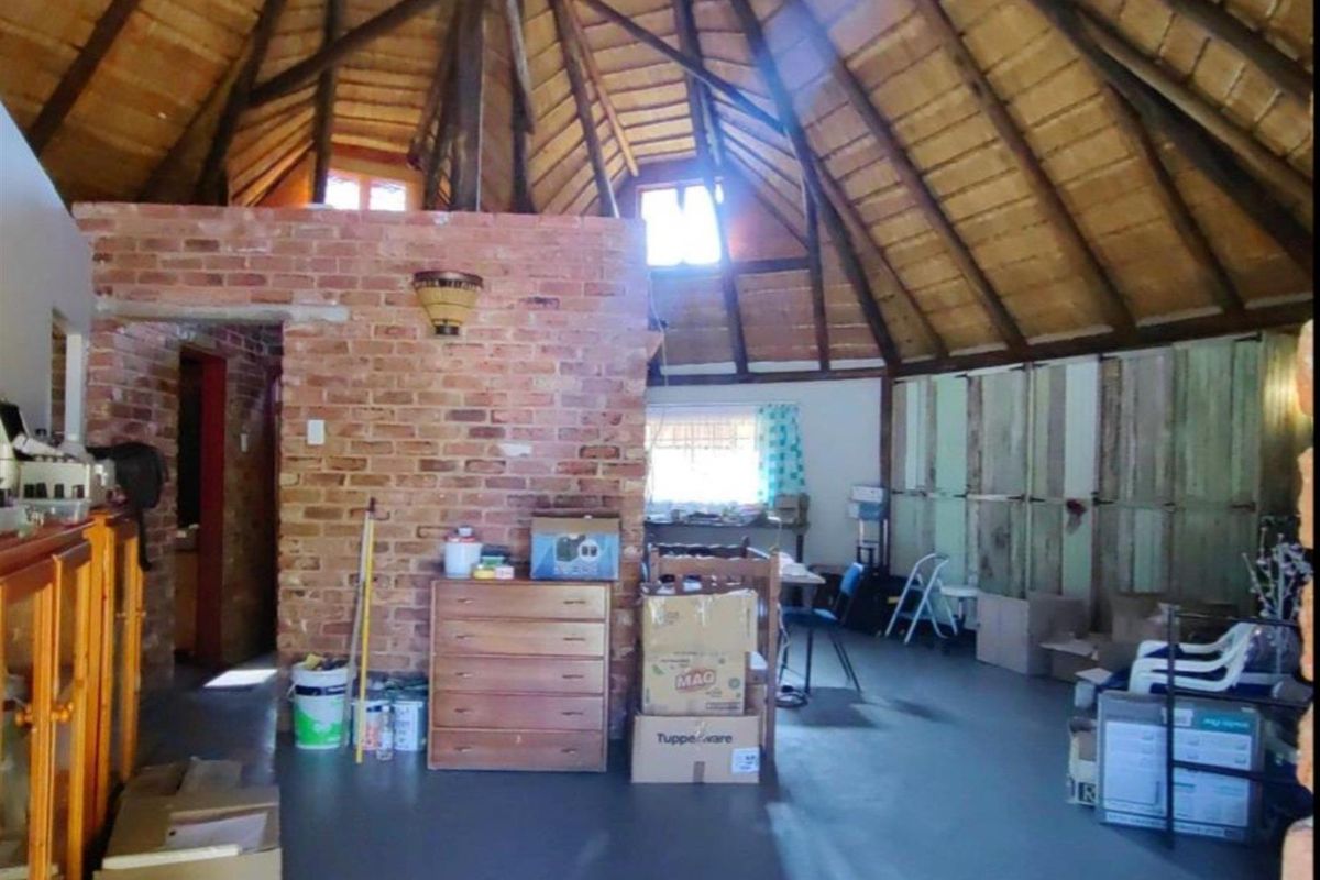 Spacious interior area featuring a high vaulted thatched roof, exposed brick feature wall, and concrete flooring, offering a rustic farm-style aesthetic.
