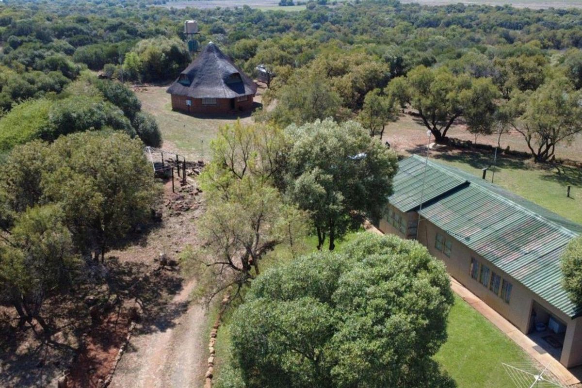 Aerial view of the farm property featuring a traditional thatched-roof structure and a main building with a green corrugated metal roof set in woodland.