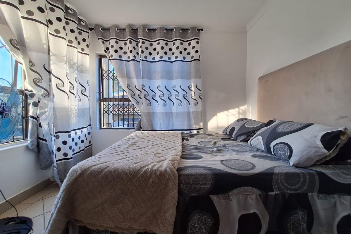 A bedroom featuring tiled flooring, a built-in headboard, and security bars on the windows.