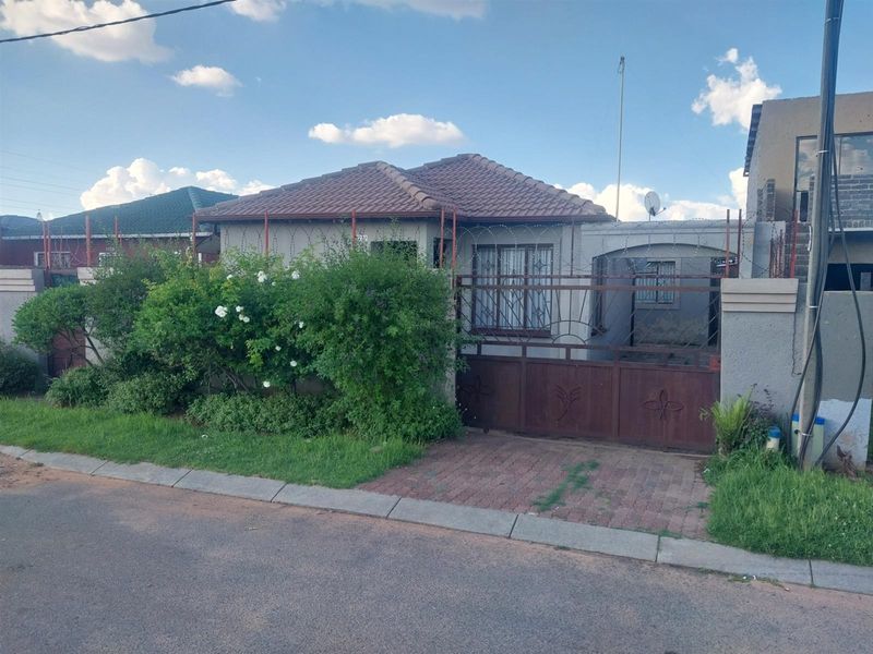 Front view of a single-story house featuring a tiled roof, paved driveway, and secure metal perimeter fencing with razor wire.