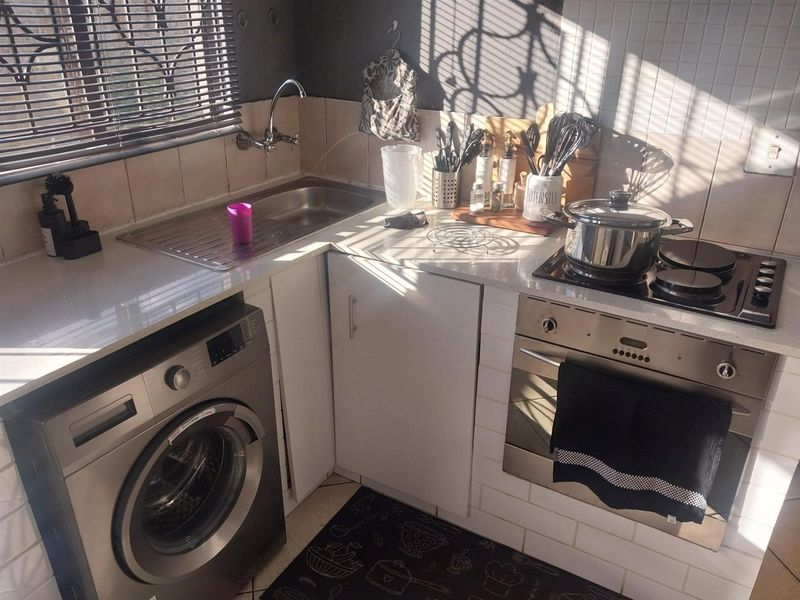 Compact kitchen featuring a stainless steel sink, built-in oven, electric hob, and integrated laundry appliance space with tiled splashbacks.