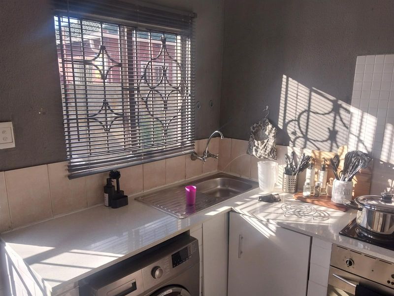 A compact kitchen area featuring a stainless steel sink, built-in oven, hob, and space for a washing machine with tiled splashbacks.