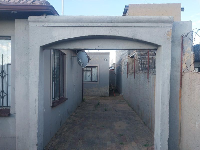A side passage or driveway area featuring a concrete archway, paved ground, and perimeter security fencing.