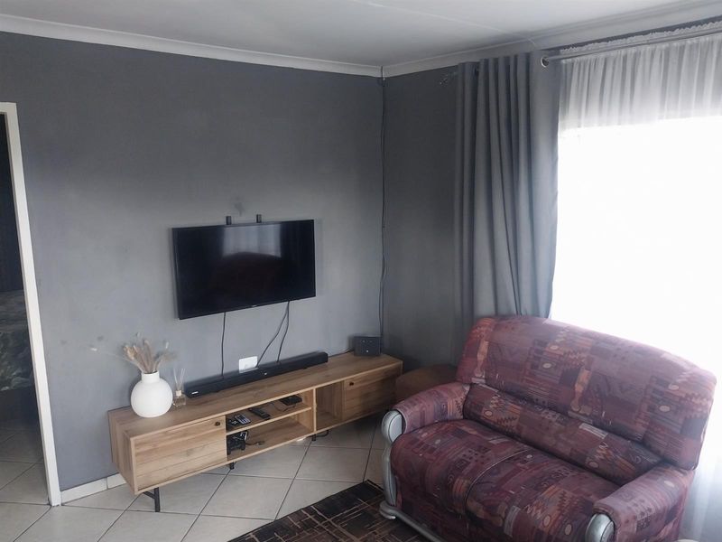 A living room featuring tiled flooring, grey painted walls, and a window with curtains.