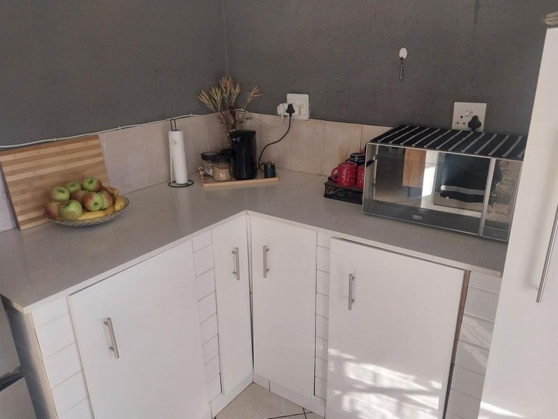 A compact kitchen corner featuring white cabinetry, light-toned countertops, and tiled splashbacks, providing functional storage and preparation space.