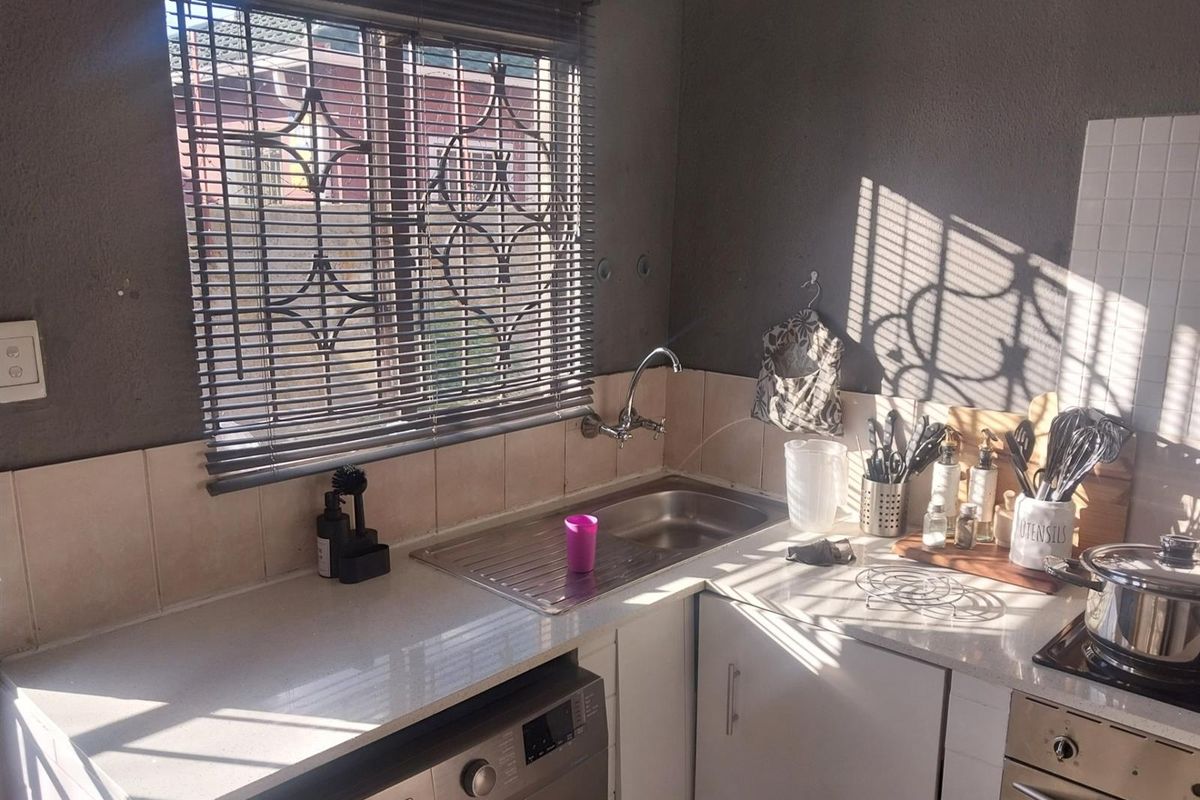 A compact kitchen area featuring a stainless steel sink, built-in oven, hob, and space for a washing machine with tiled splashbacks.