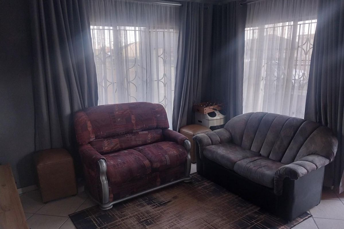A living room featuring tiled flooring, large windows with security bars, and floor-to-ceiling curtains, providing a functional and well-lit space.