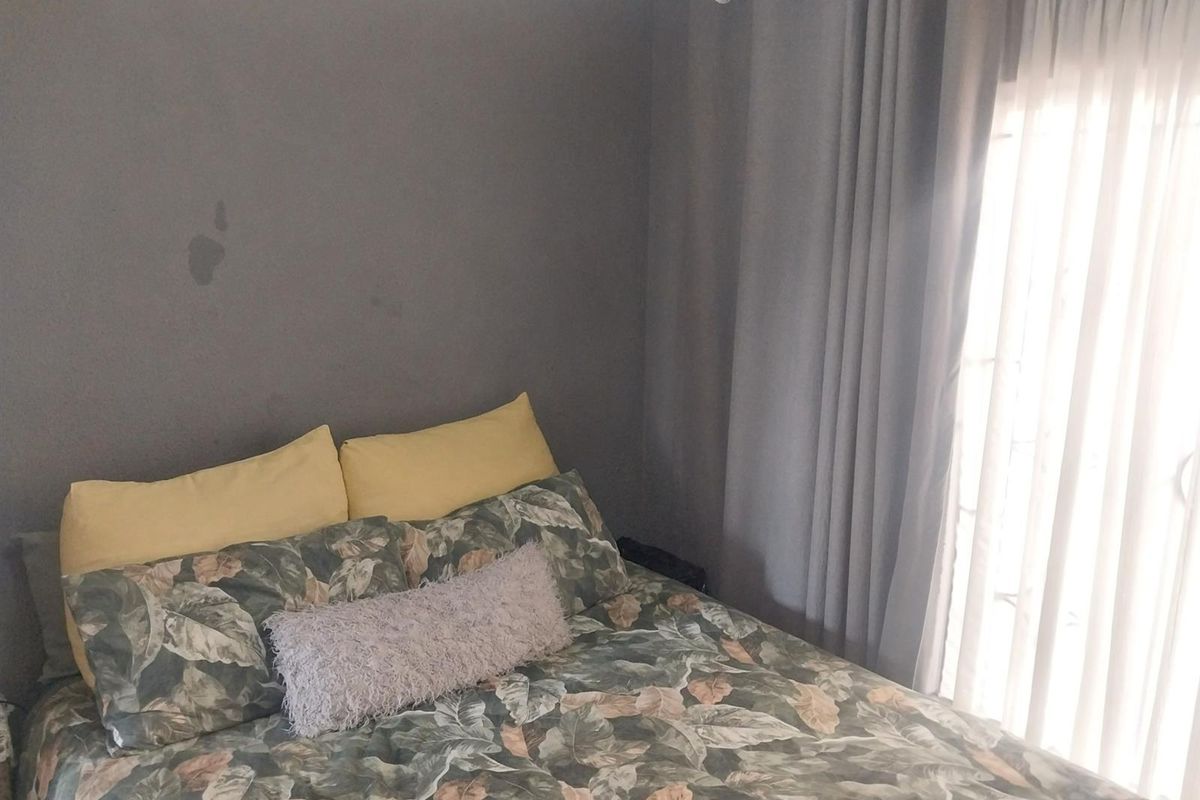 A bedroom featuring grey painted walls, a sliding door with curtains, and neutral flooring.