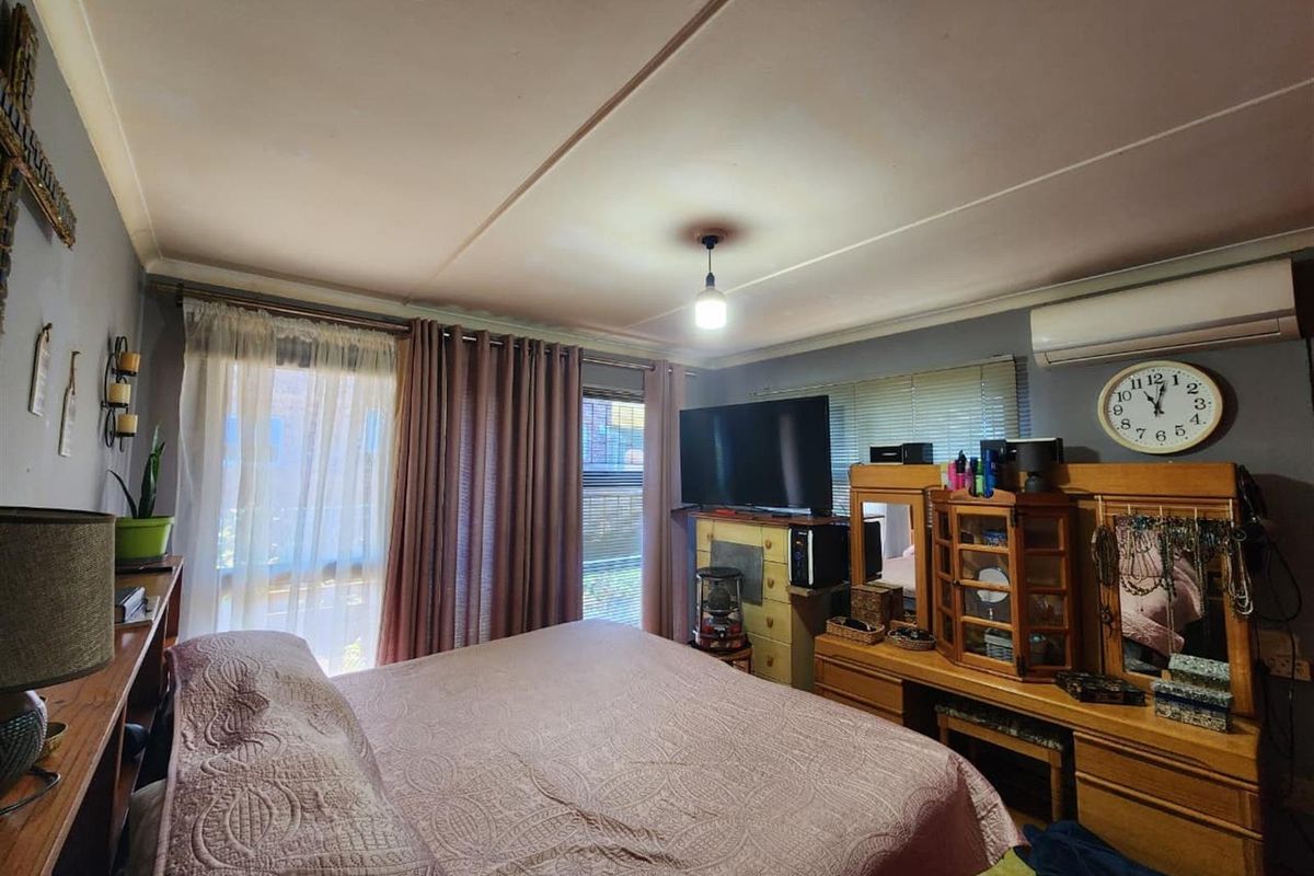 A bedroom featuring a wall-mounted air conditioning unit and large windows with curtains, providing natural light and climate control.