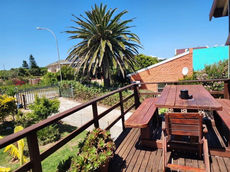 An elevated wooden deck patio featuring timber railings, overlooking a landscaped garden and driveway area.