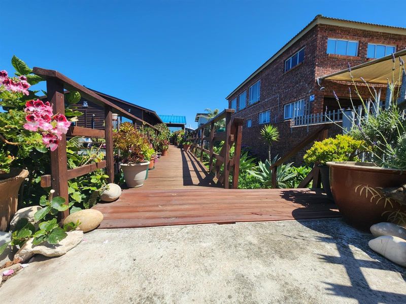 A wooden walkway bridge leading between two residential buildings, featuring timber railings and landscaped garden borders.