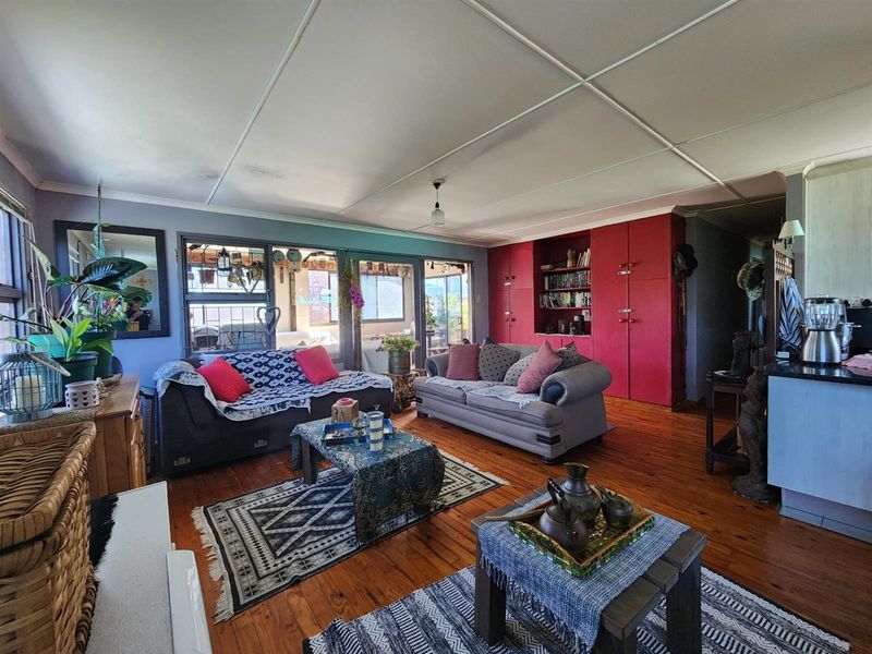 Spacious open-plan living area featuring polished timber flooring, built-in red cabinetry, and large windows providing natural light and access to the adjacent patio.