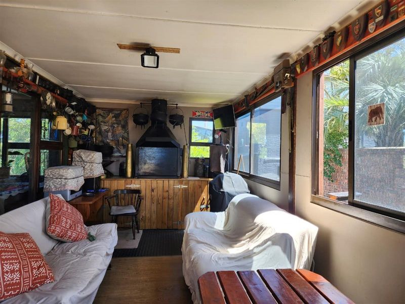 A rustic enclosed patio or entertainment area featuring a built-in indoor braai, wooden cabinetry, and large windows overlooking the garden.