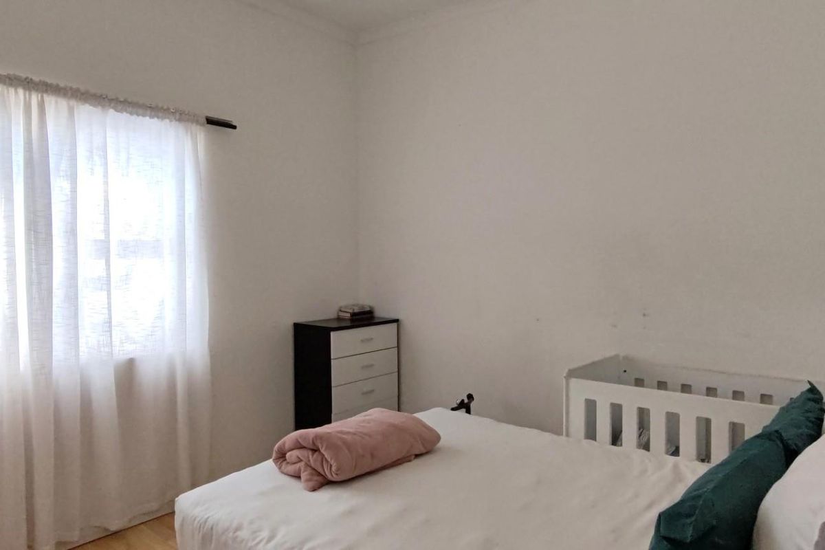 A simple bedroom featuring white walls, a window with a curtain rod, and light-colored flooring.