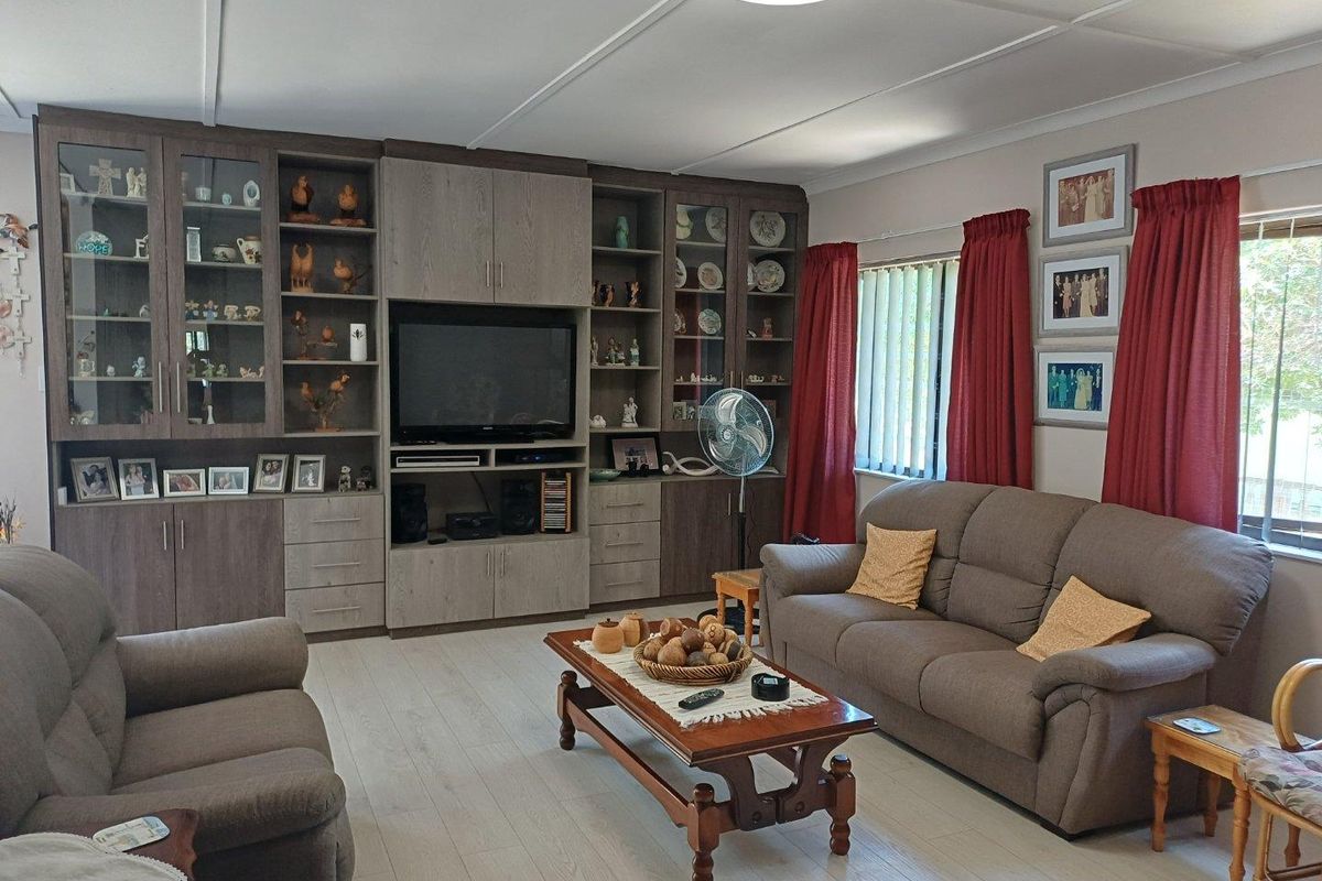 A comfortable living room featuring extensive built-in cabinetry with integrated shelving and display units, complemented by light-toned flooring and vertical blinds.