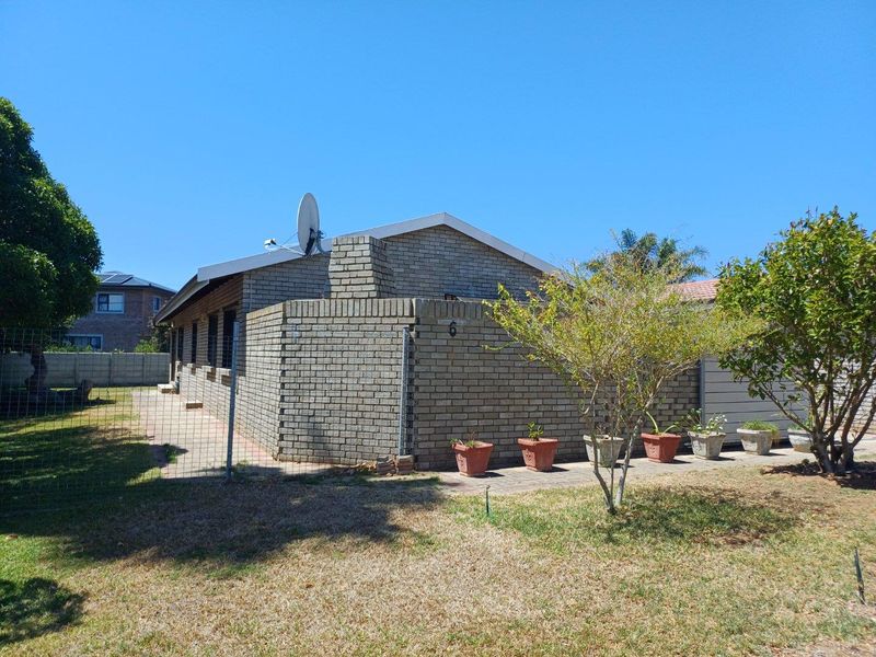 A view of the side and rear exterior of a face-brick house featuring a paved walkway and established garden area.