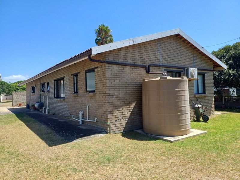 Side elevation of a brick-built house featuring a rainwater storage tank, external air conditioning unit, and guttering system set within a grassed yard.