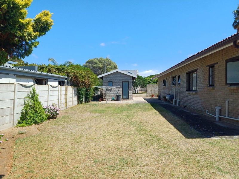 A spacious rear garden featuring a brick-built outbuilding, paved walkway, and perimeter walling, offering potential for landscaping and outdoor living improvements.