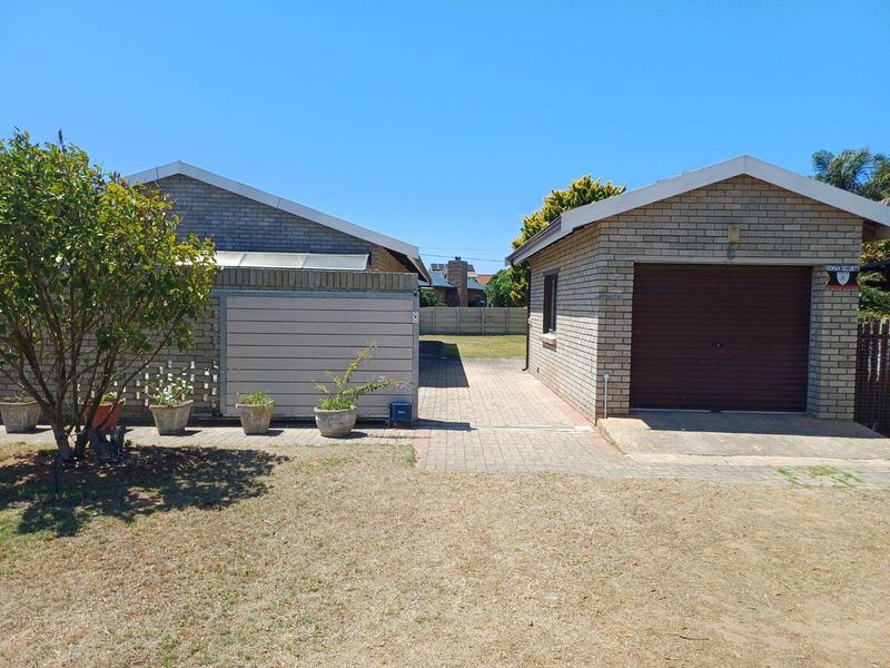 Exterior view of a brick-built garage and adjacent structure with paved driveway and surrounding garden area.