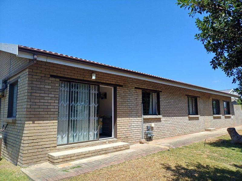 A rear exterior view of a single-story brick house featuring a sliding glass door with security gate and paved walkway.