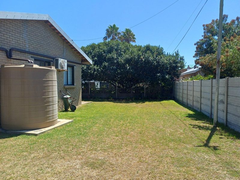 A private rear garden featuring a level lawn, perimeter concrete walling, and a large water storage tank attached to the side of the house.