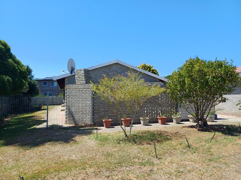 A view of the rear exterior of the house featuring face brick walls, a paved patio area, and a surrounding garden.