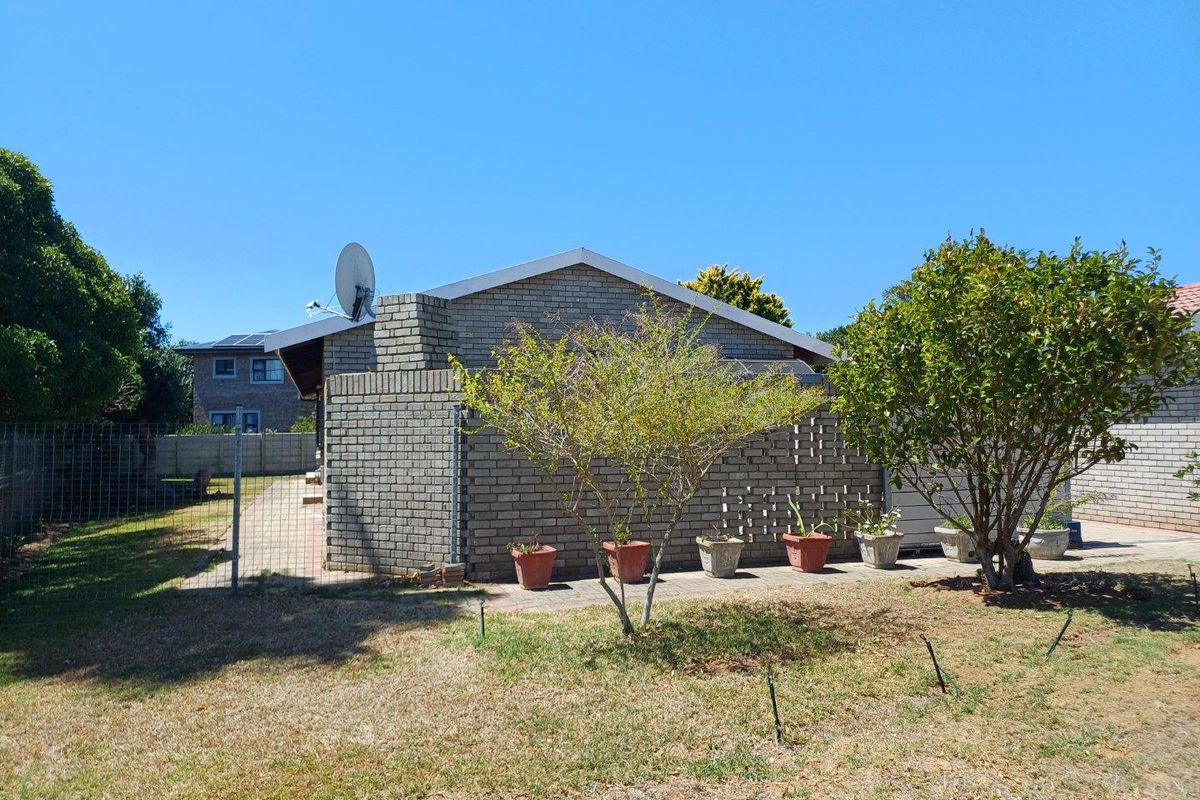 A view of the rear exterior of the house featuring face brick walls, a paved patio area, and a surrounding garden.