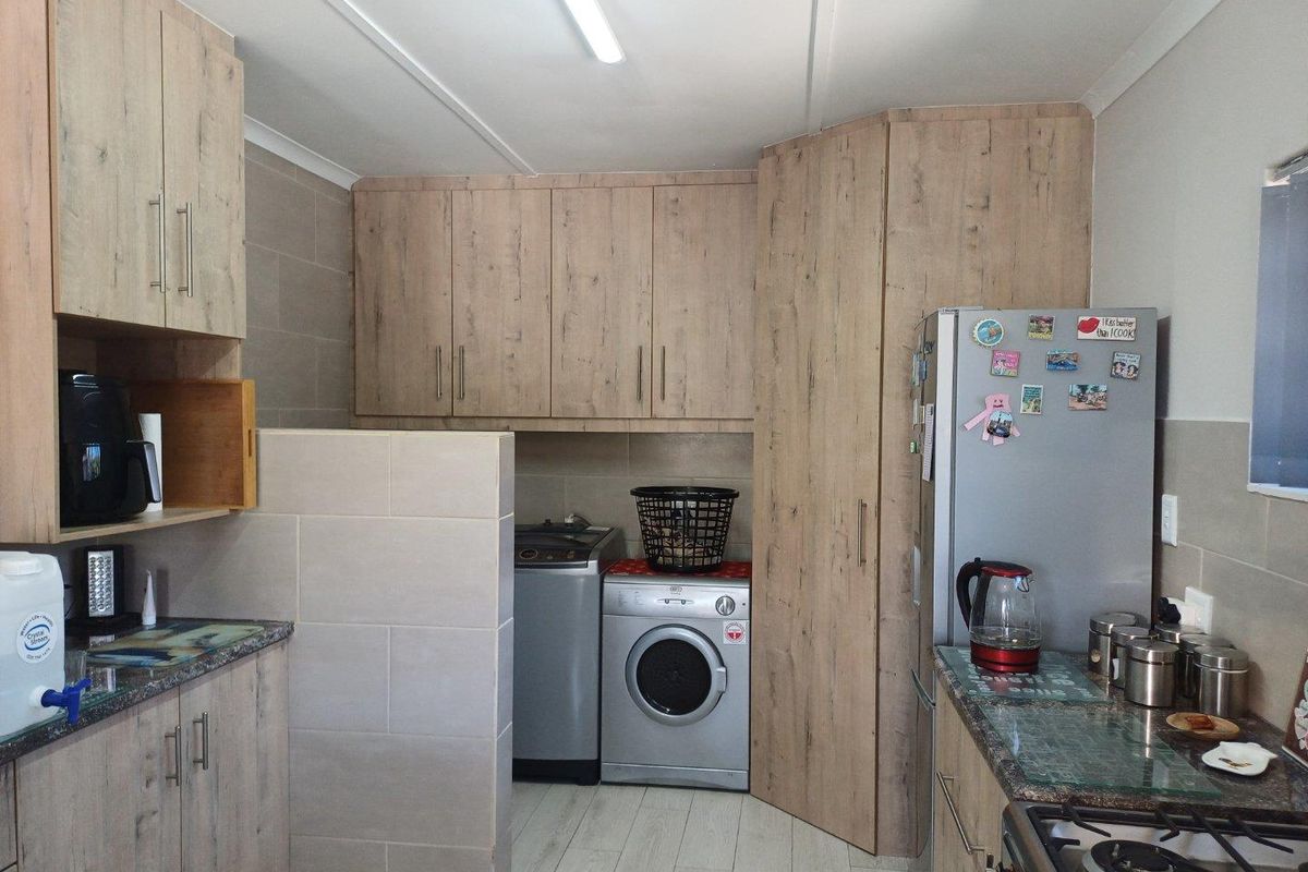 A functional kitchen and laundry area featuring wood-look cabinetry, tiled splashbacks, and integrated space for laundry appliances.