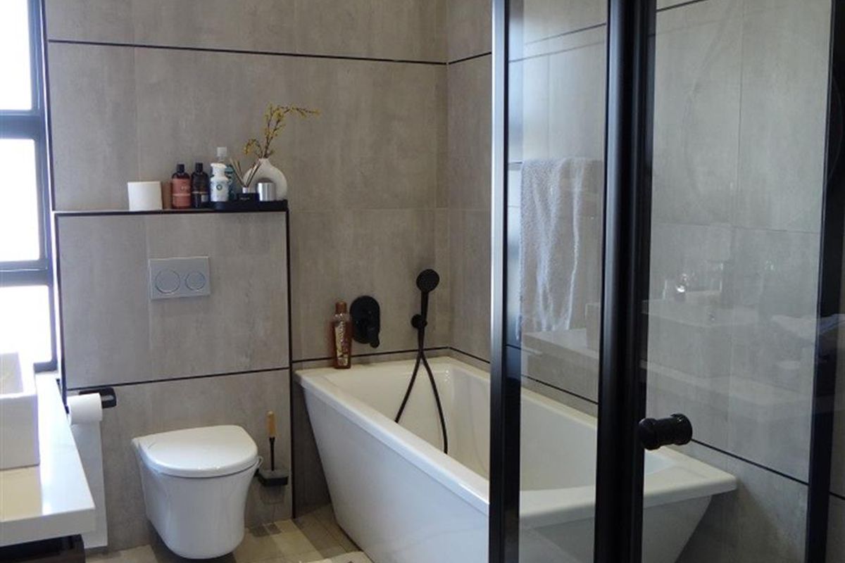 Modern bathroom featuring large-format grey wall tiles, a wall-hung toilet, a sleek freestanding bathtub, and a glass-enclosed shower with black frame detailing.