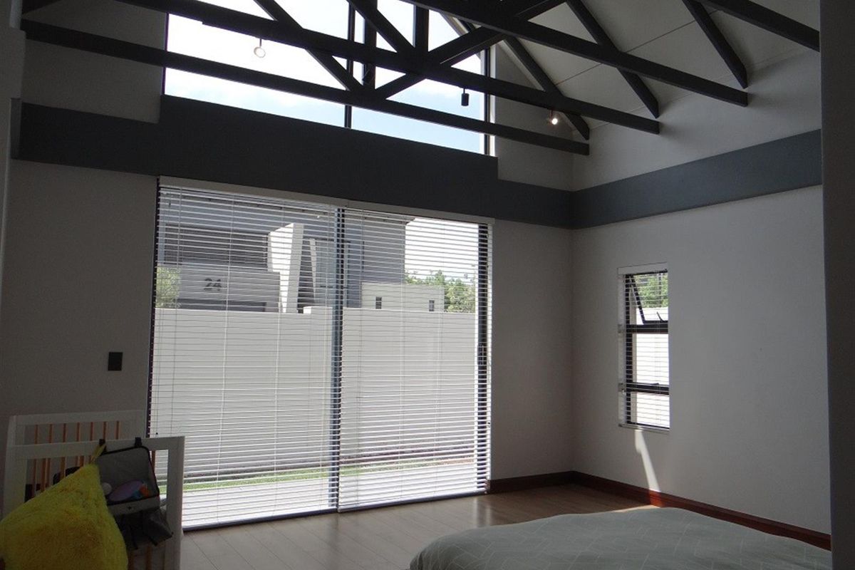 Spacious bedroom featuring high vaulted ceilings with exposed timber trusses, large sliding glass doors, and timber flooring.