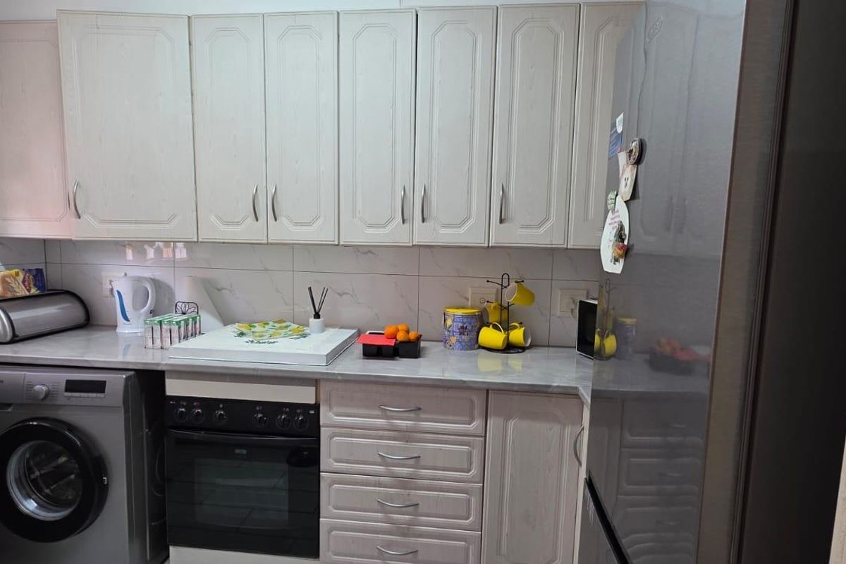 A functional kitchen featuring light-toned cabinetry, marble-effect countertops, tiled backsplash, and a built-in oven with an integrated laundry appliance space.