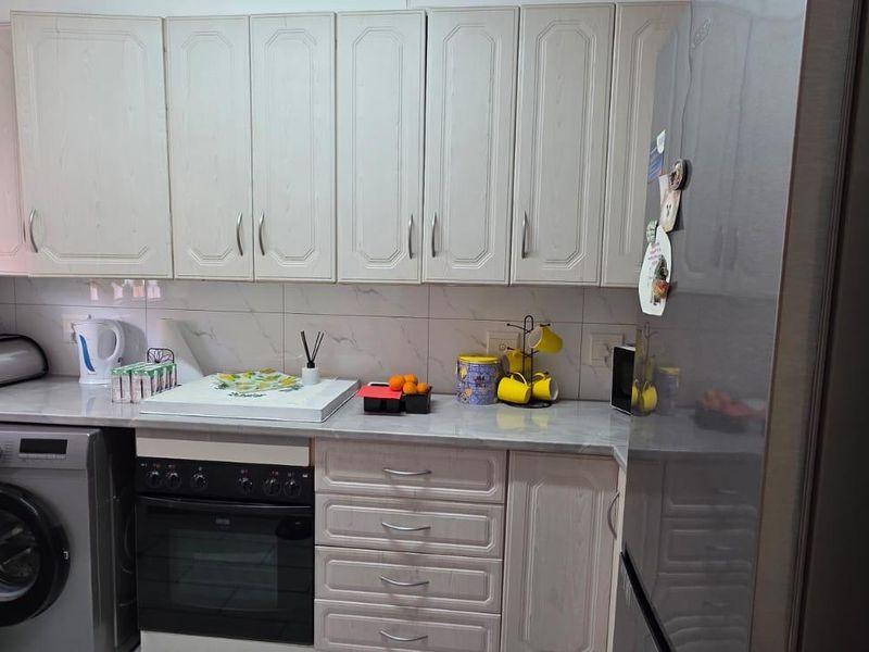 A functional kitchen featuring light-toned cabinetry, marble-effect countertops, tiled backsplash, and a built-in oven with an integrated laundry appliance space.