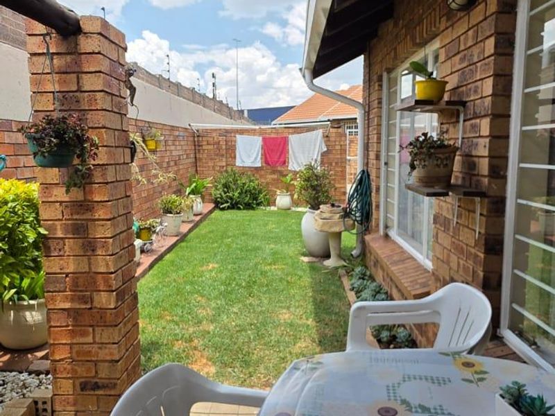 A private rear garden featuring a paved patio area with a shade sail, brick boundary walls, and a well-maintained lawn.
