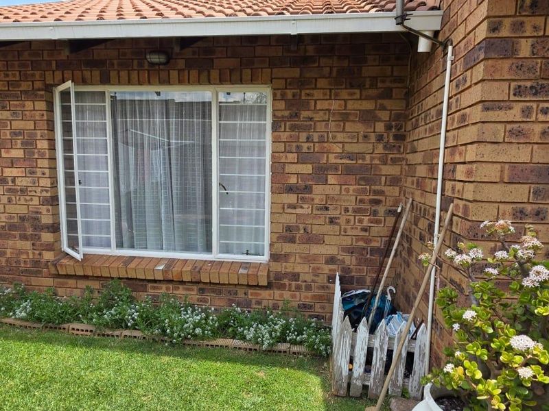 A view of the exterior rear brick facade featuring a window with security bars, overlooking a small garden area.