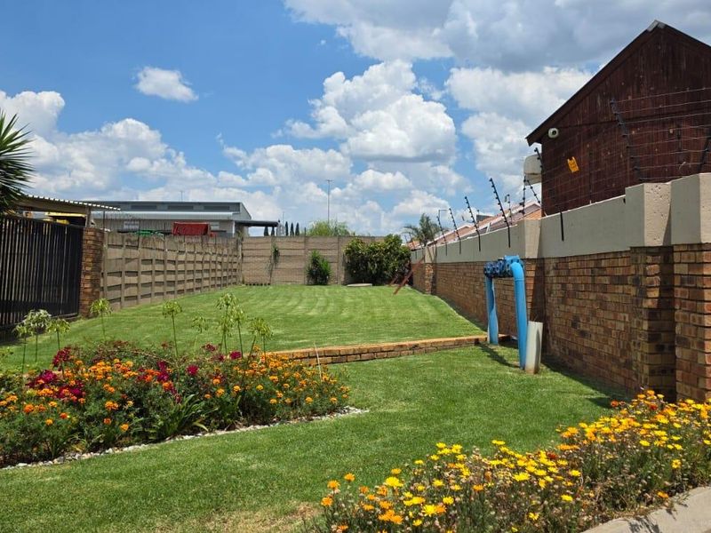 A well-maintained rear garden featuring a manicured lawn, established flower beds, and secure perimeter brick walling with electric fencing.
